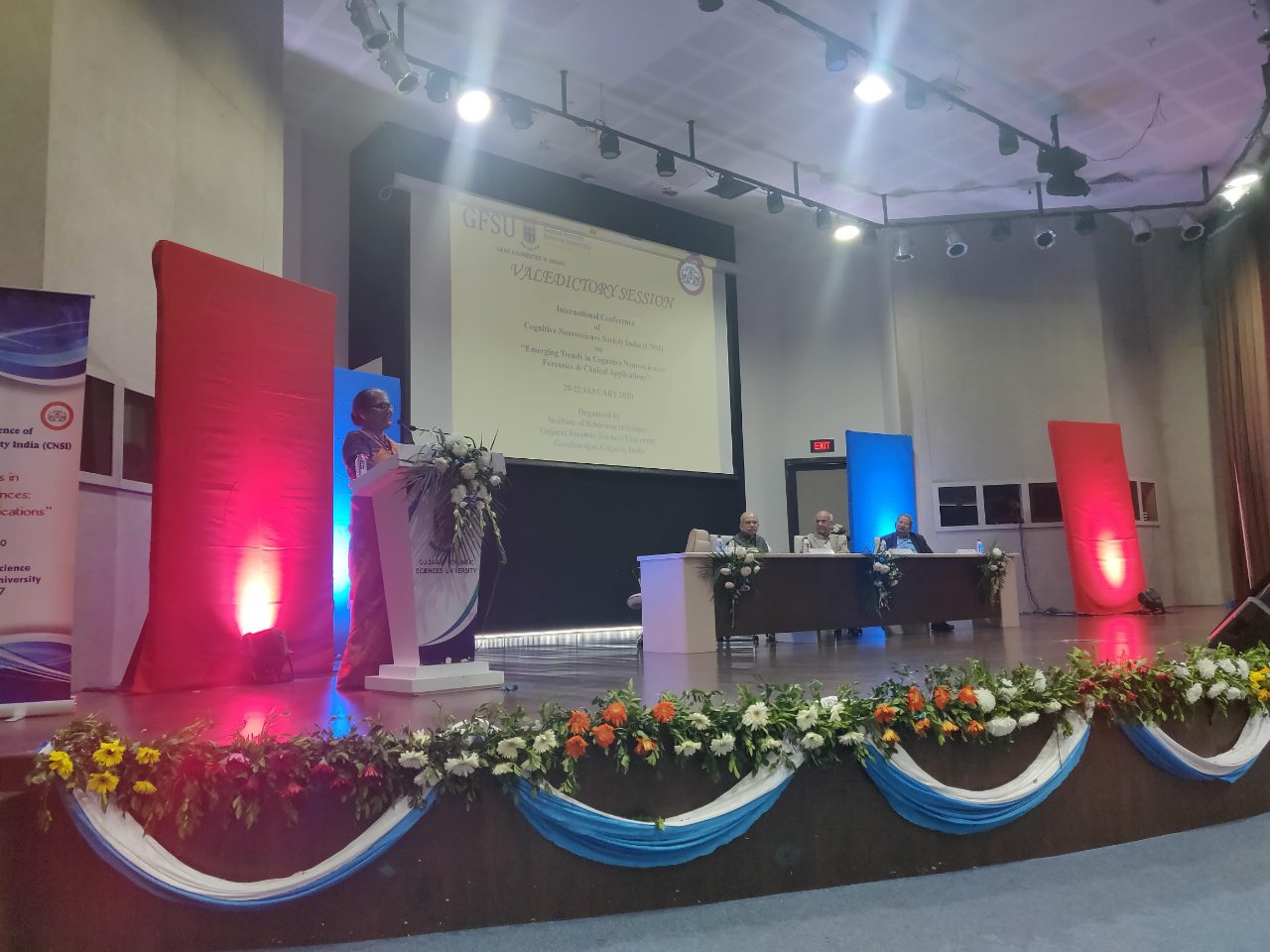 A speaker addresses the valedictory session from the lectern, three guests seated on the dais