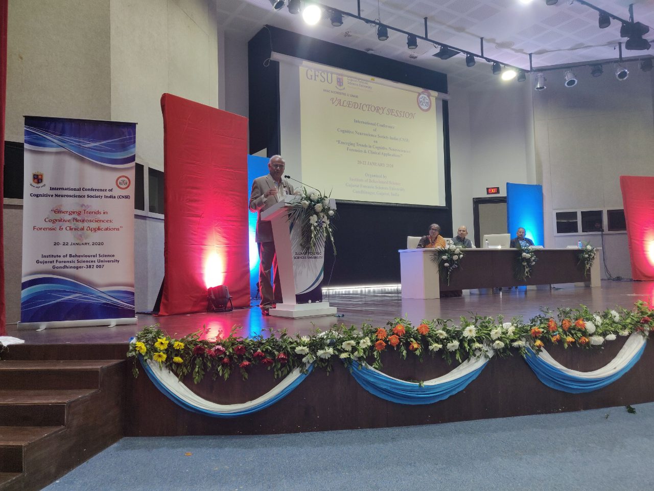 Another address in the valedictory session, the CNSI-2020 banner at left and three guests on the dais