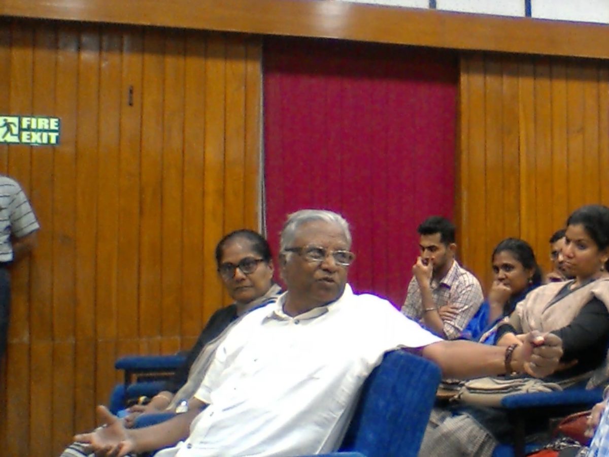 A listener in the front row makes a point in the discussion after a talk at NIMHANS, others looking on