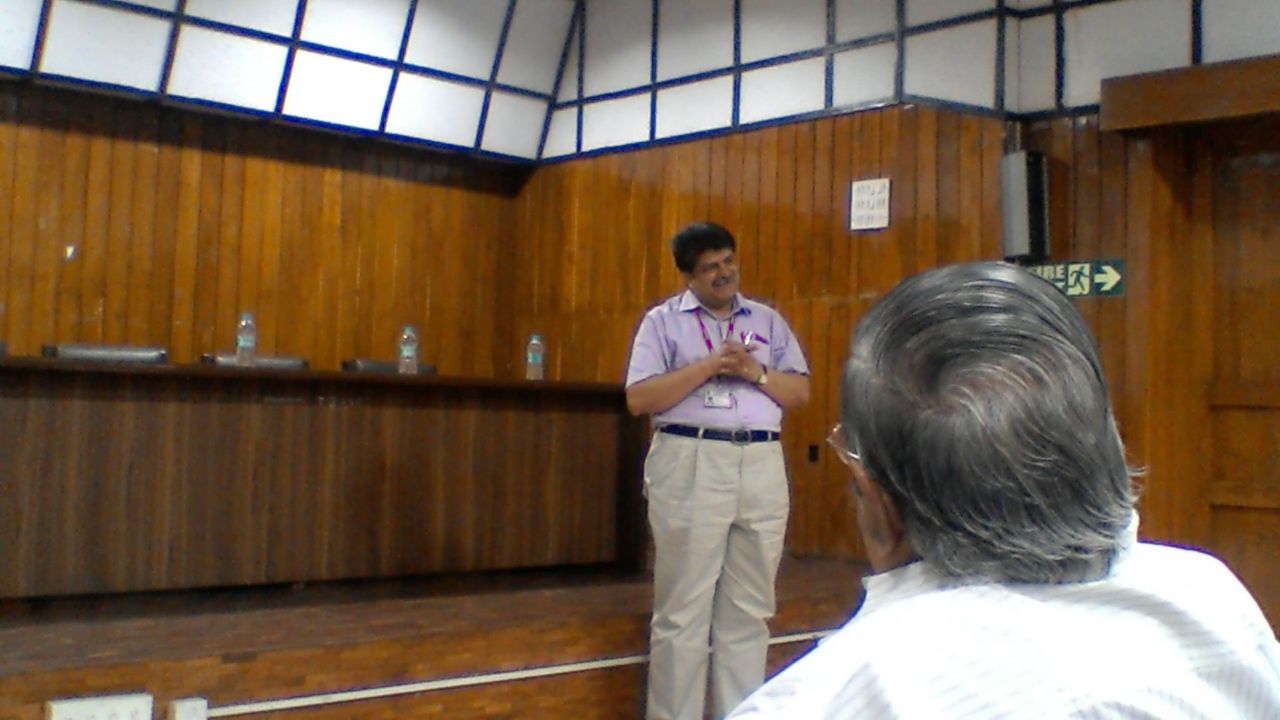 The same man, hands clasped and smiling, in front of the dais