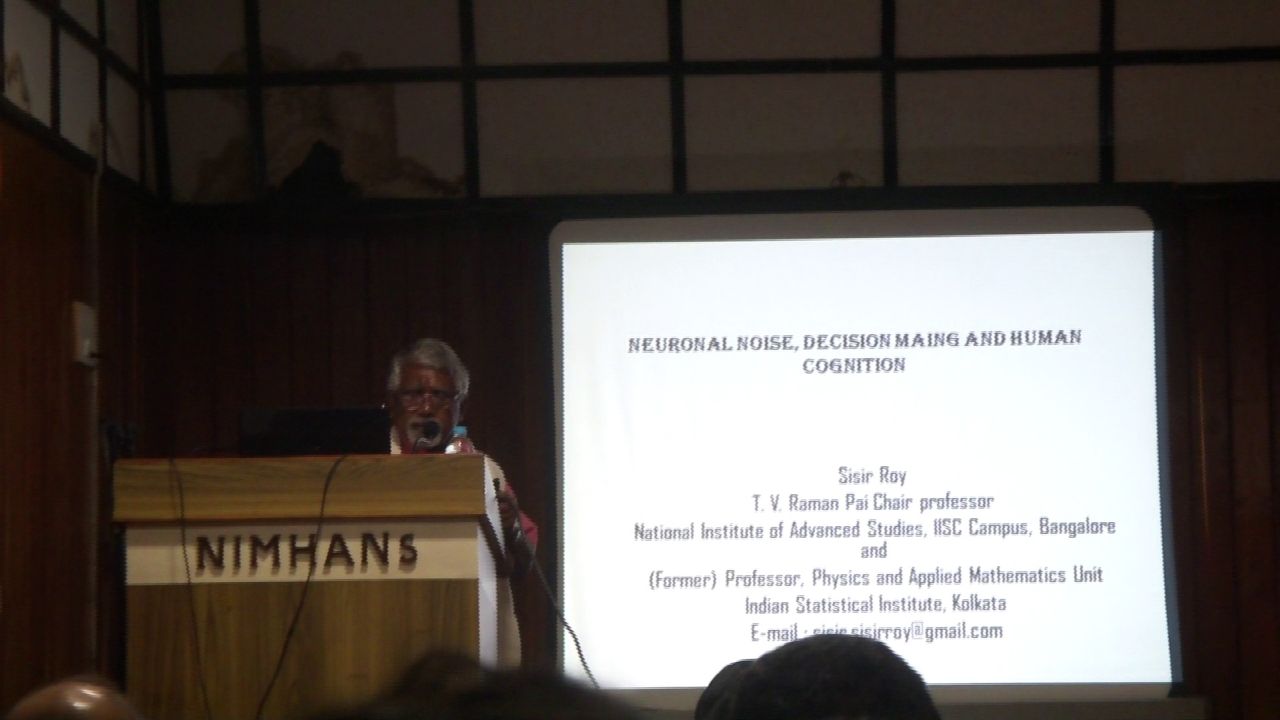 Prof. Sisir Roy at the NIMHANS lectern beside his title slide, ‘Neuronal noise, decision making and human cognition’